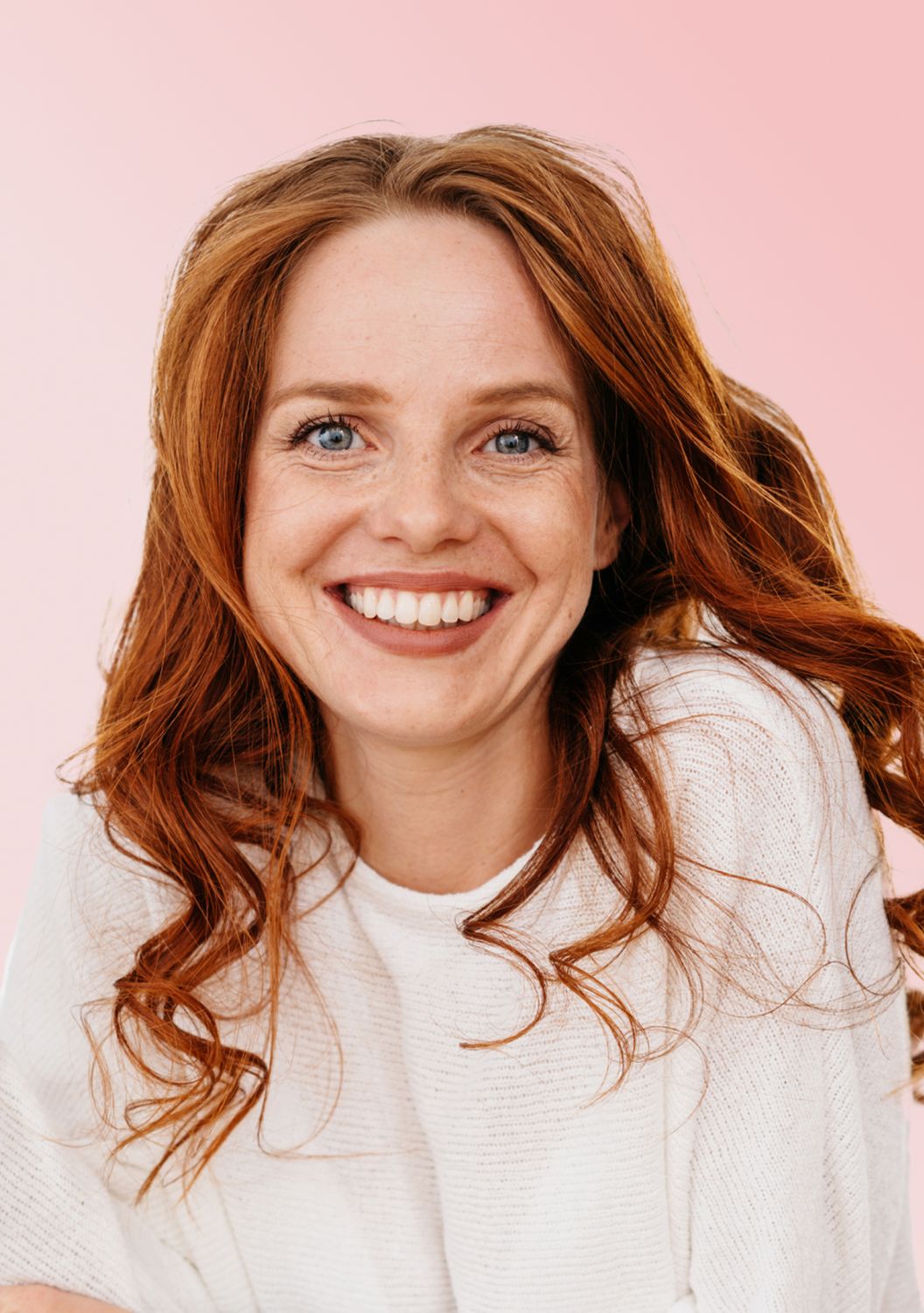 Smiling woman with red hair on pink background.