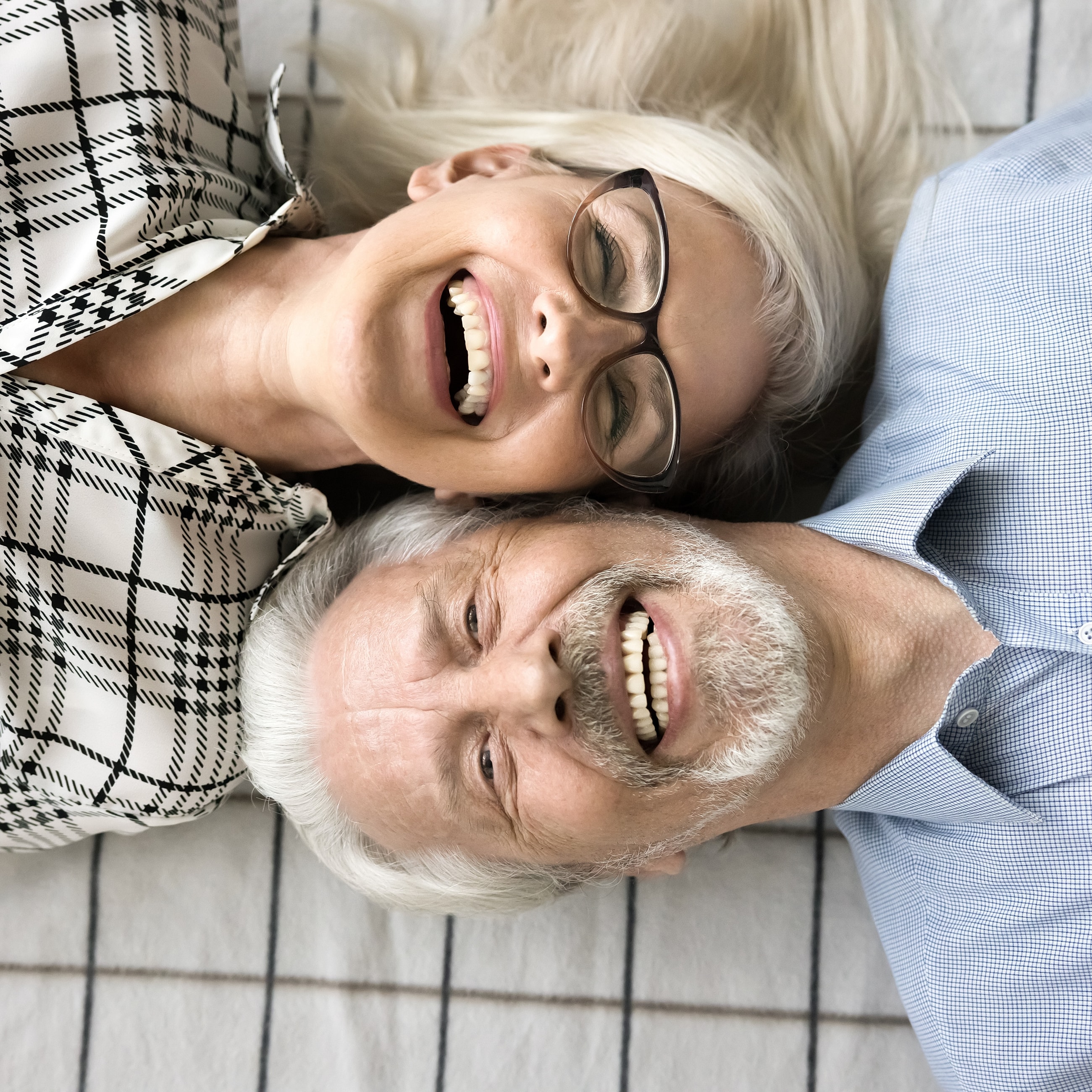 Smiling couple lying together on a blanket with full-mouth dental implants