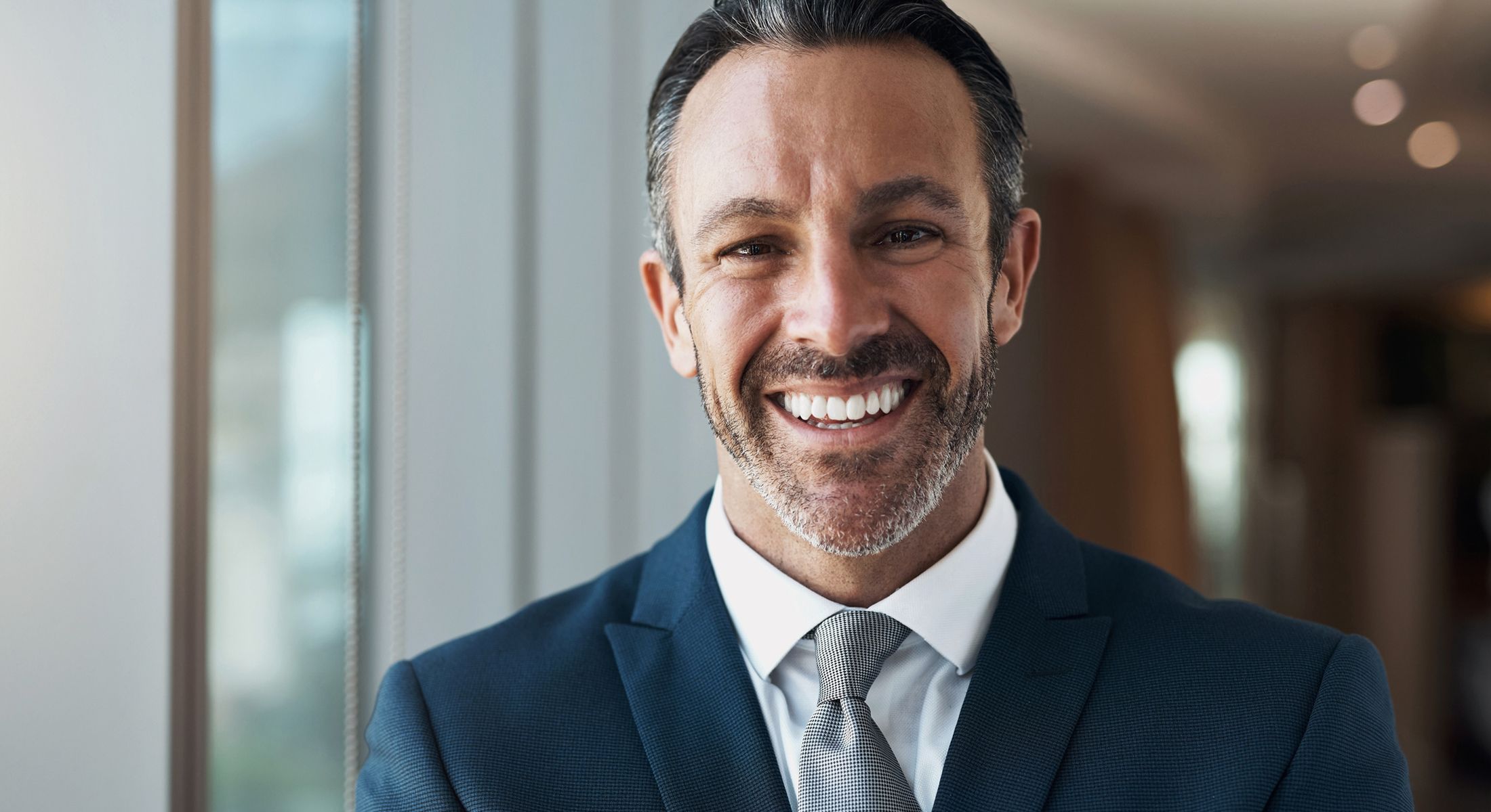 Smiling businessman in a suit near window.