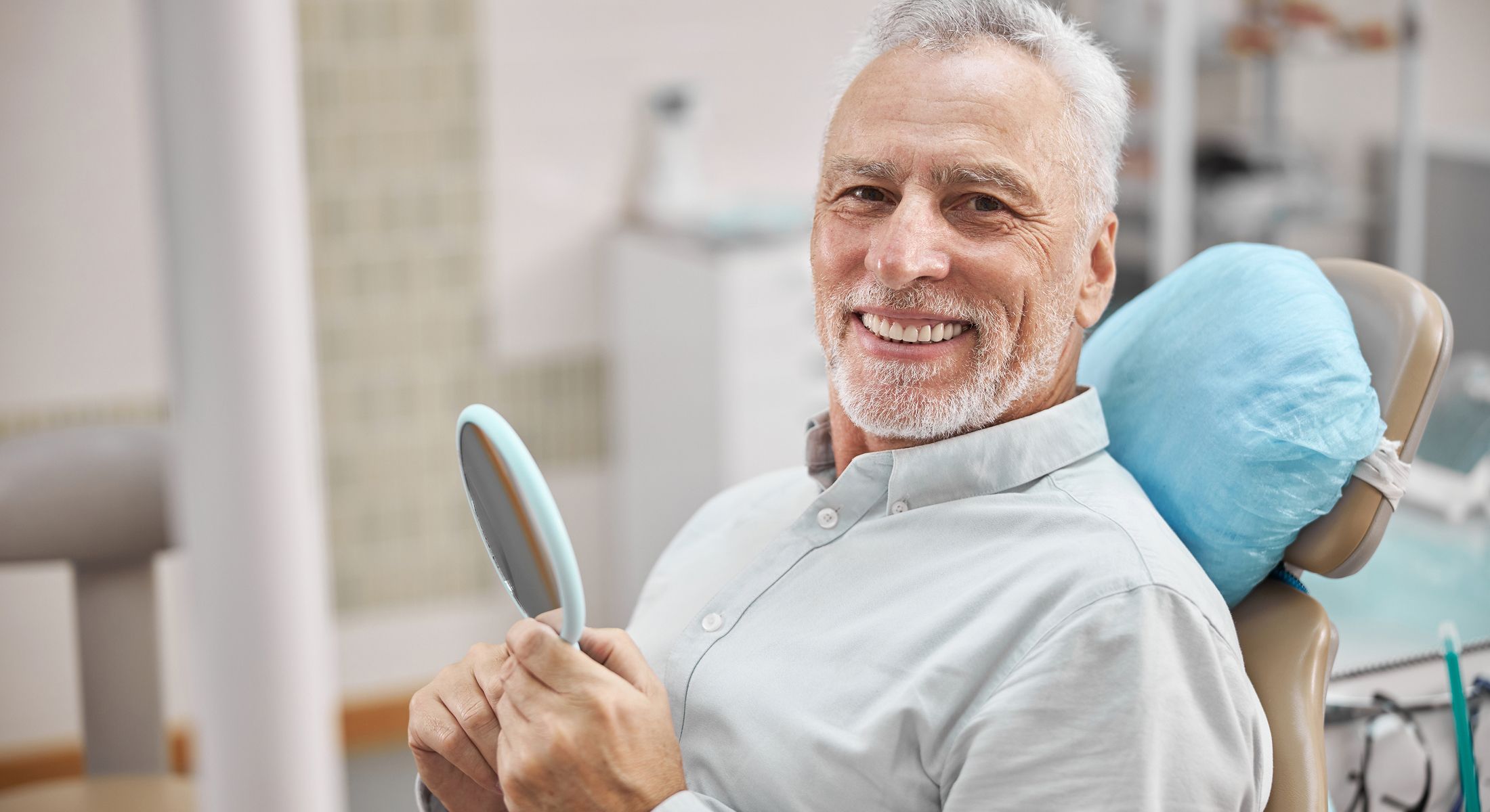 Smiling patient in dental chair holding mirror.